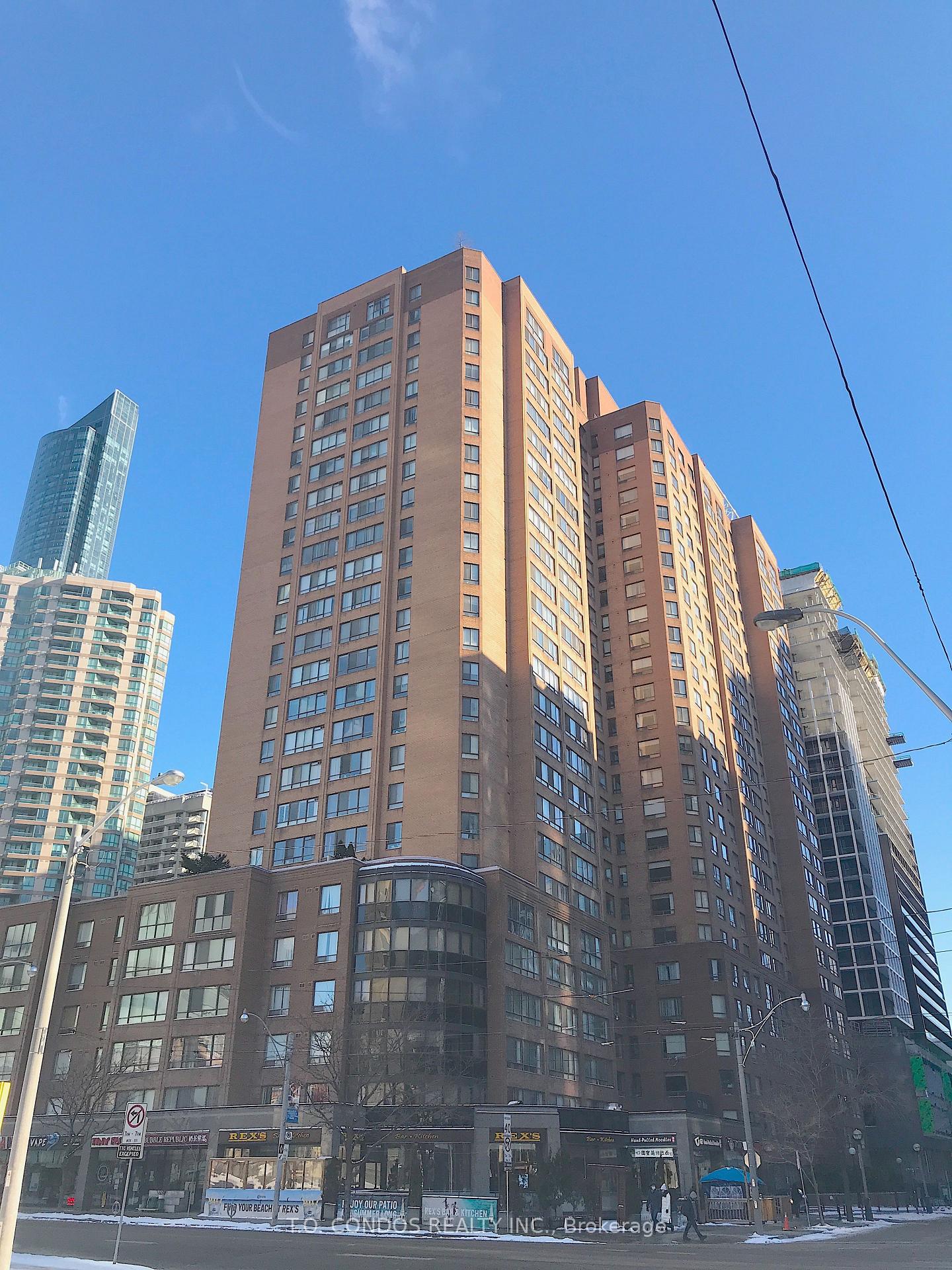 Brown brick condominium tower with storefronts at street level, framed by neighboring high-rises.