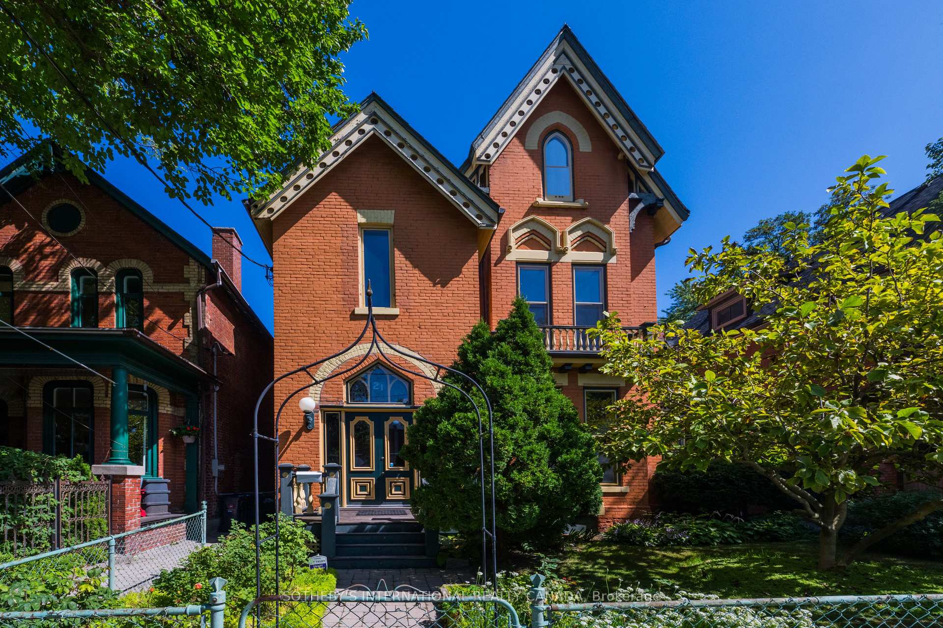 Red-brick Victorian house with ornate gables, a dark front door, and a leafy garden.