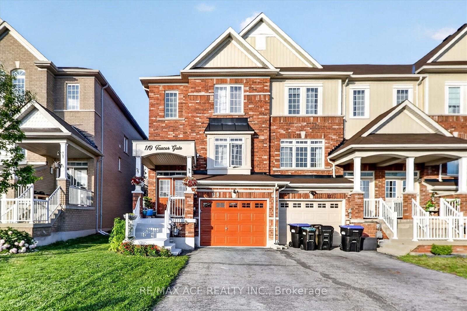 Red-brick attached home with an orange garage door, covered entry, and landscaped front lawn.