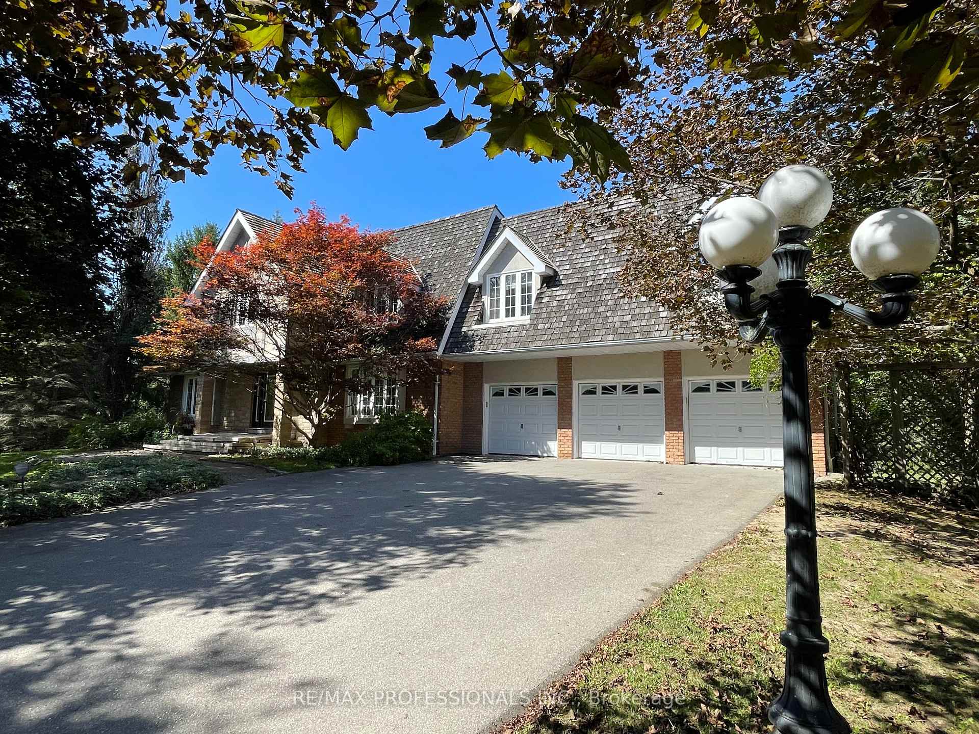 House with three garage doors and a broad driveway, framed by mature autumn trees.