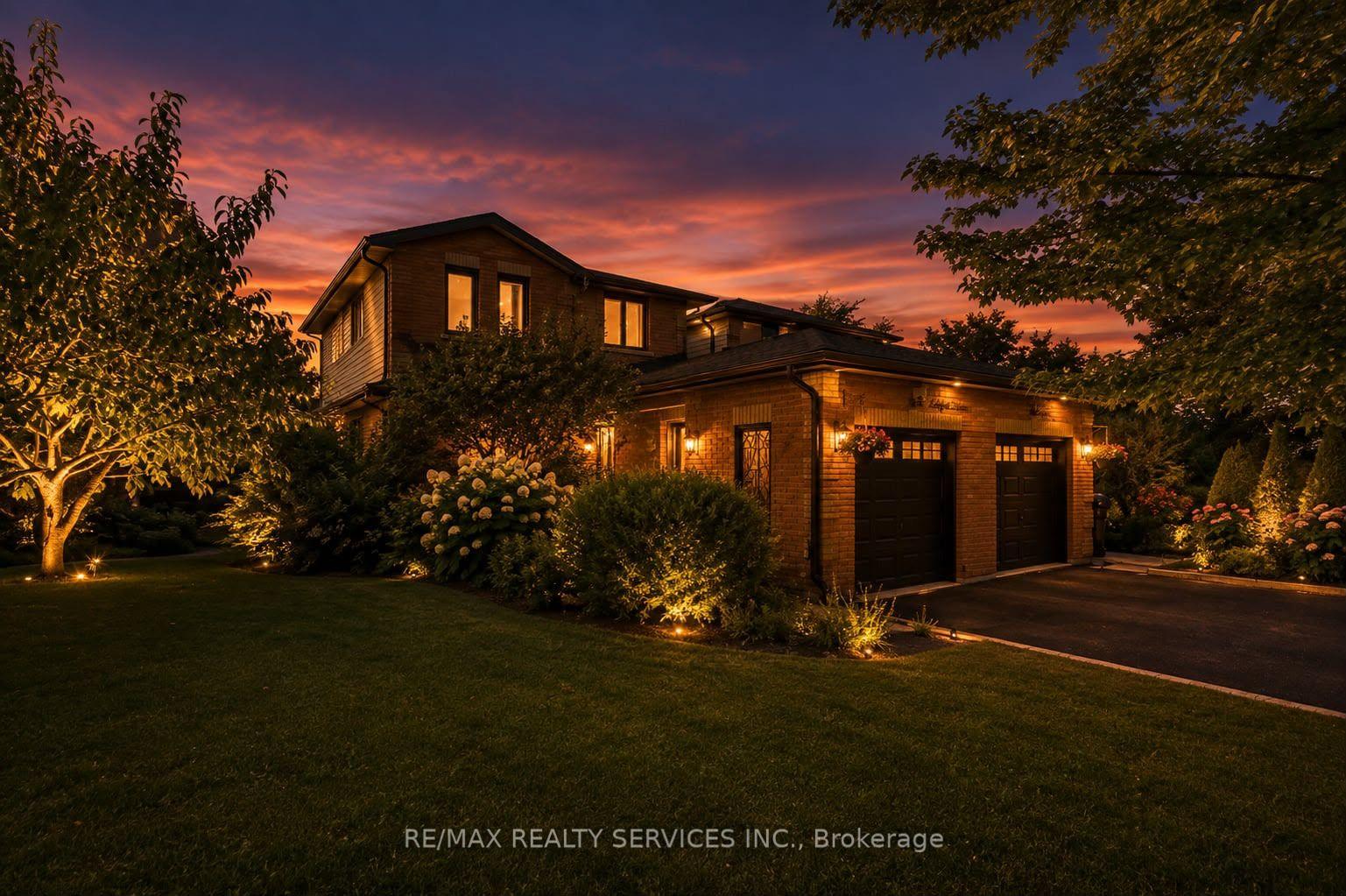 Two-story brick home with a double garage and landscaped yard glowing beneath a colorful sunset.