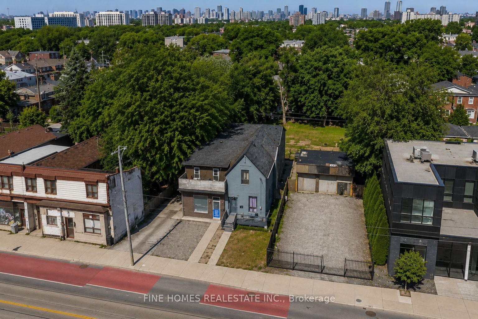 Aerial view of detached homes and a gravel driveway among mature trees, with the city skyline beyond.