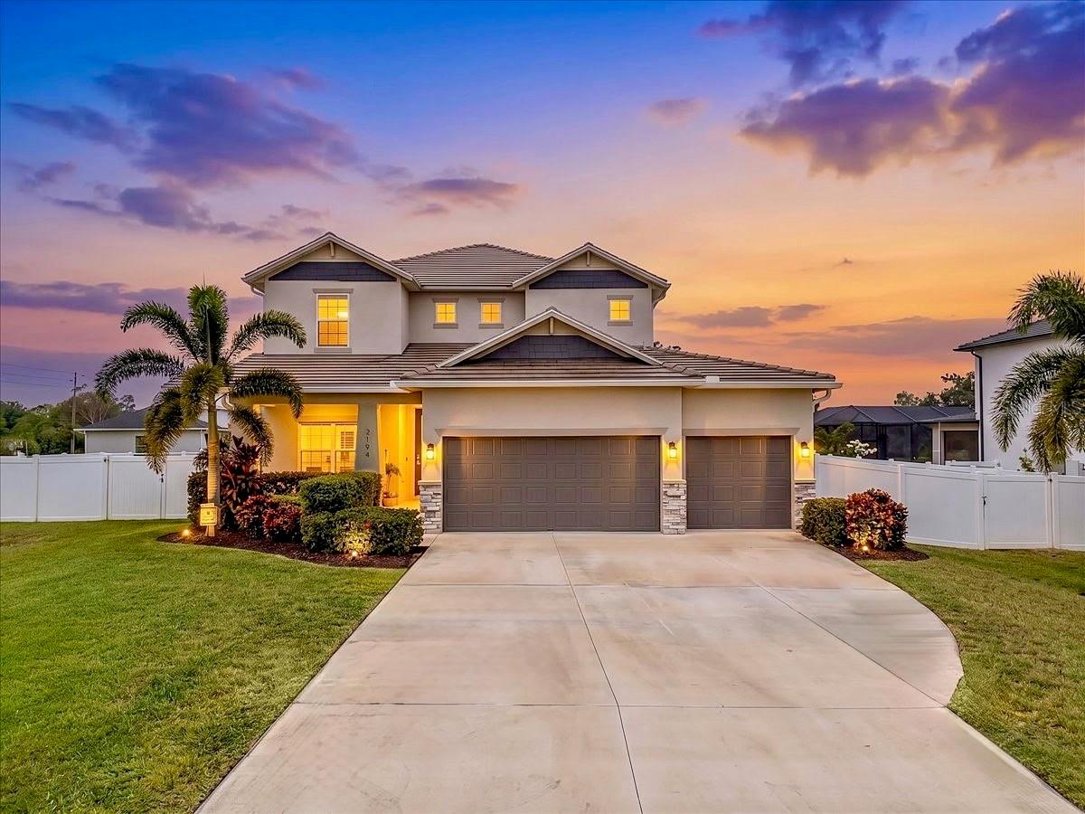 Two-story home with a three-car garage, palm landscaping, and white privacy fencing at sunset.