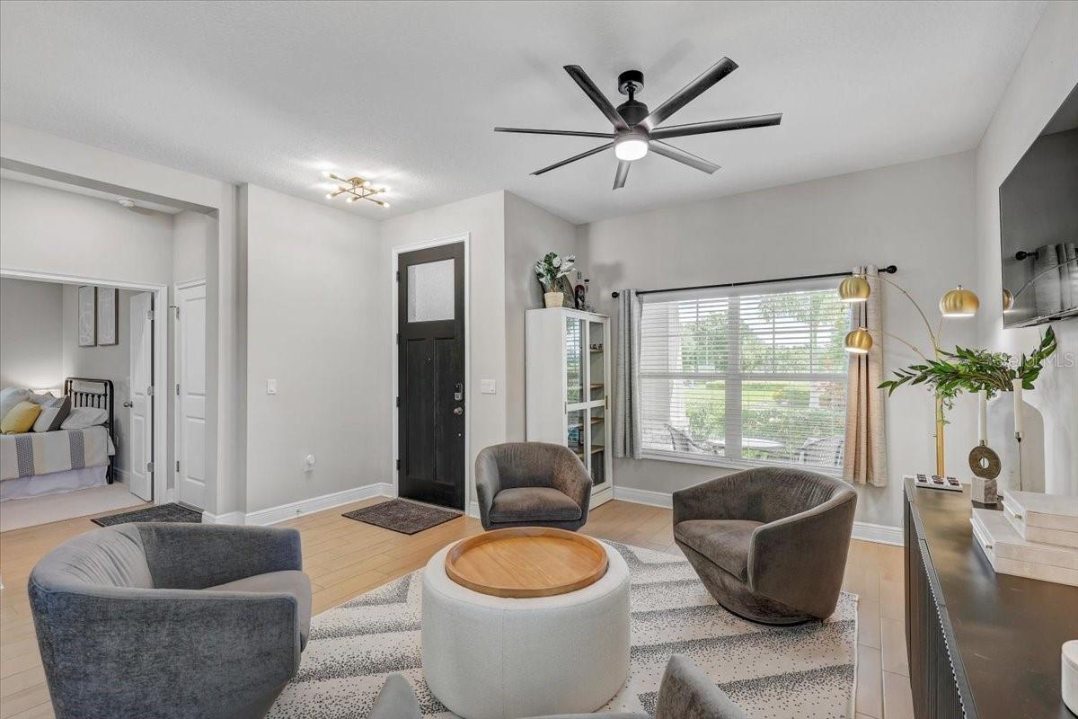 Furnished living room with gray chairs, round coffee table, large window, and black front door.