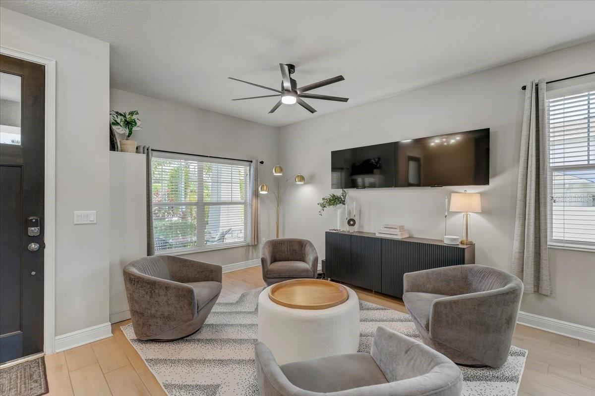Living room with gray chairs, round coffee table, wall-mounted TV, and large windows.