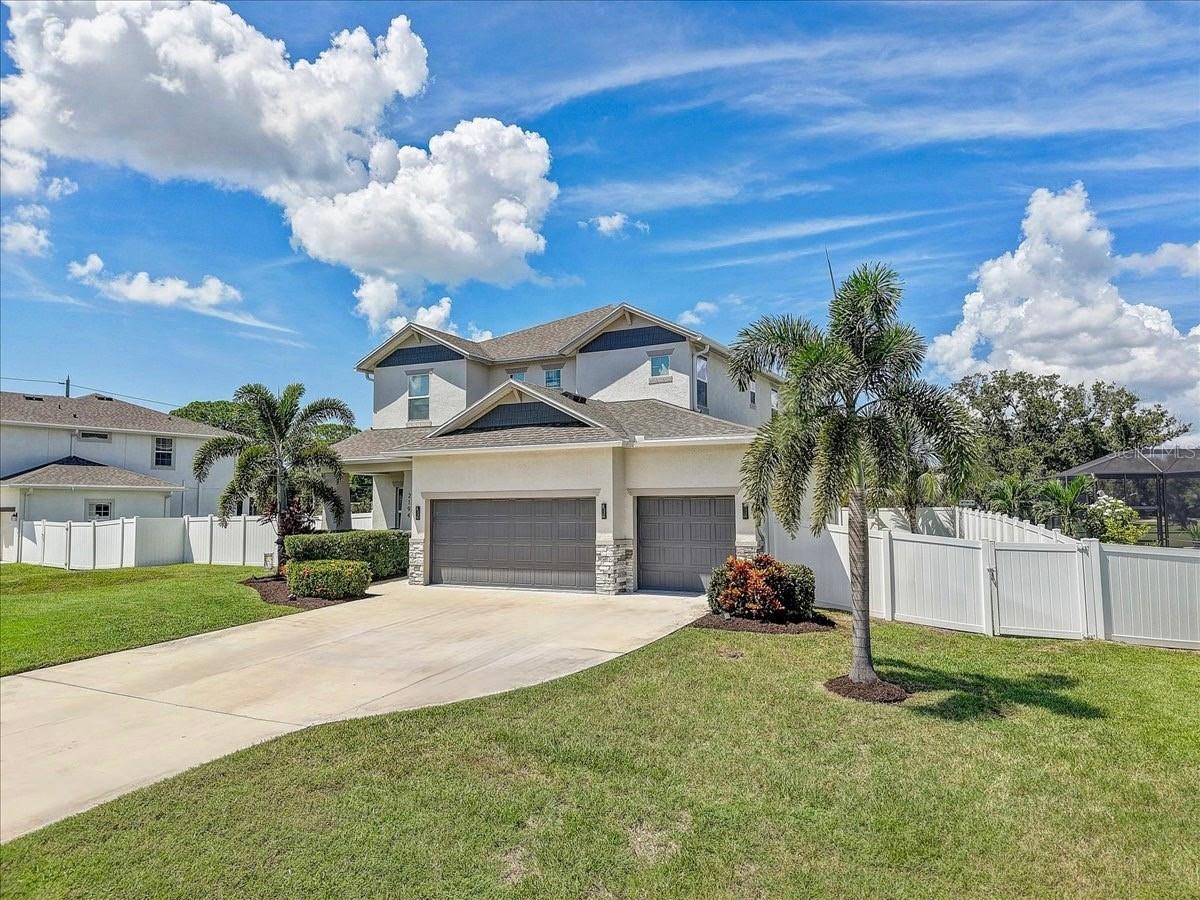 Two-story stucco home with a double garage, palm trees, white fencing, and a wide driveway.