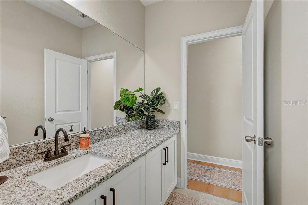 Bathroom vanity with speckled granite counter, white cabinetry, dark fixtures, and a large mirror.