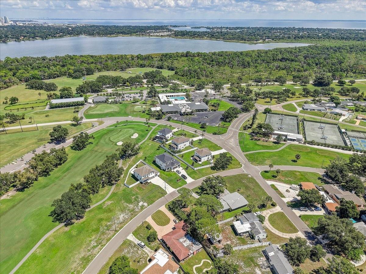 Aerial view of homes beside a golf course, with a bay and tennis courts in the distance.