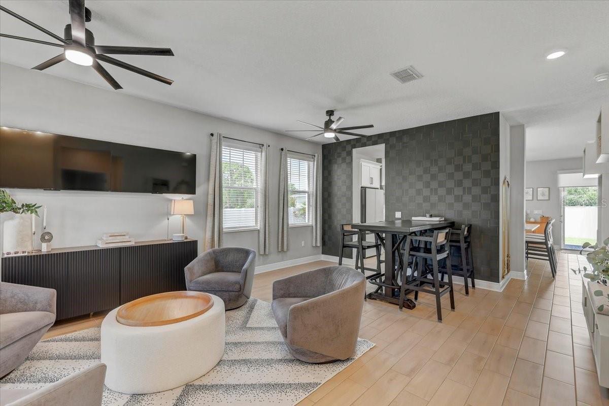 Open-plan living and dining room with a dark tiled accent wall and gray lounge chairs.