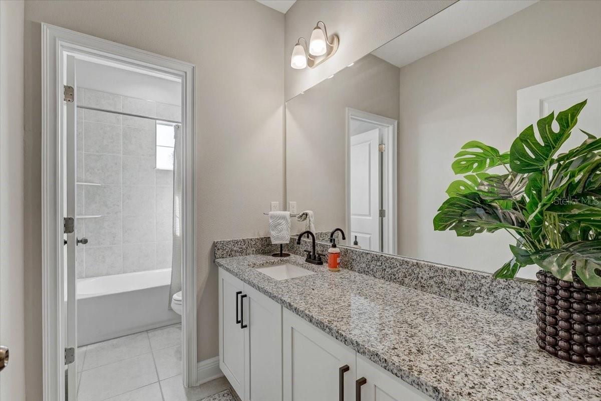 Bathroom with a granite vanity, black faucets, white cabinets, and a tiled tub and shower.