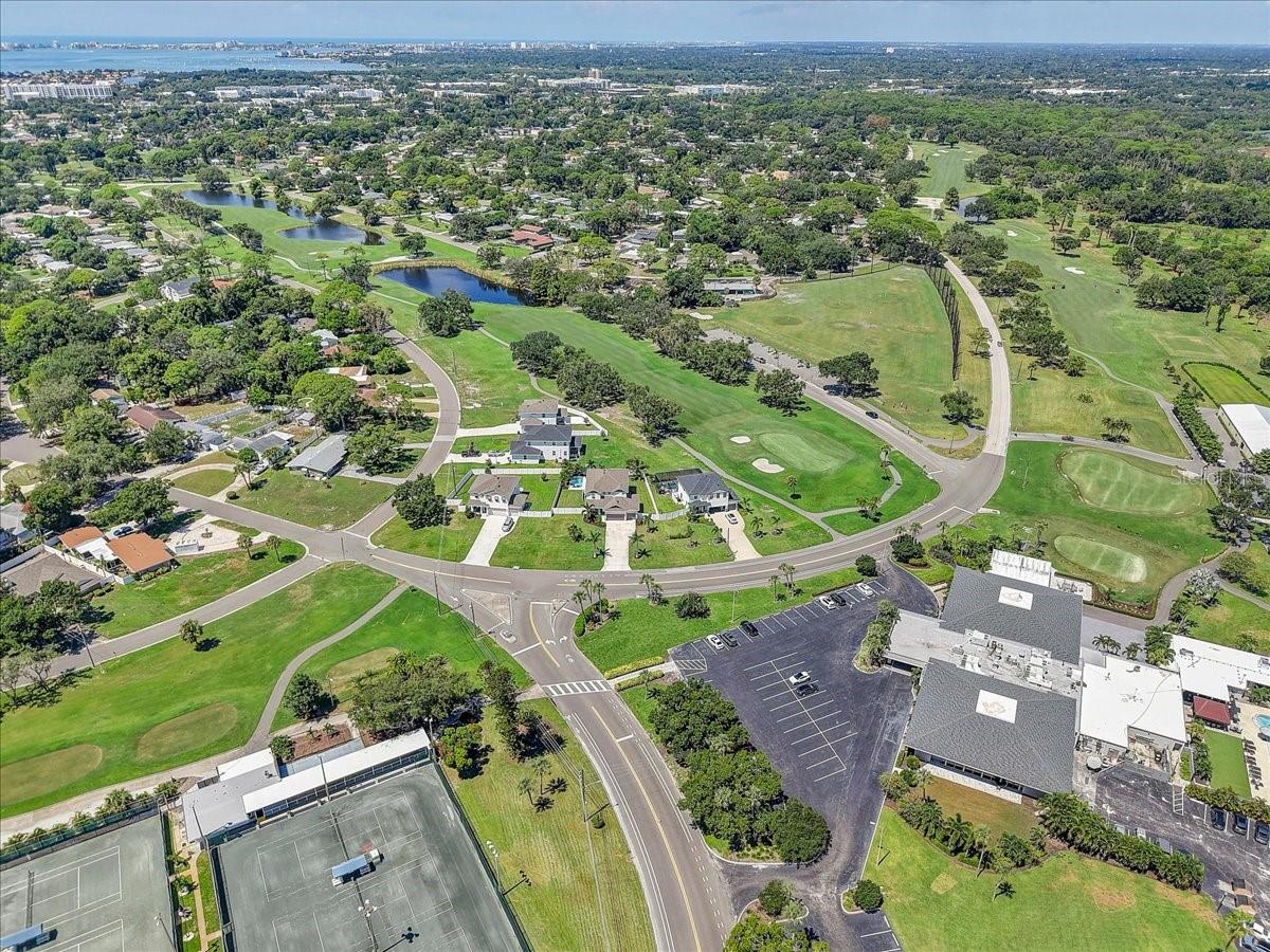 Aerial view of homes beside a golf course with ponds and tennis courts.