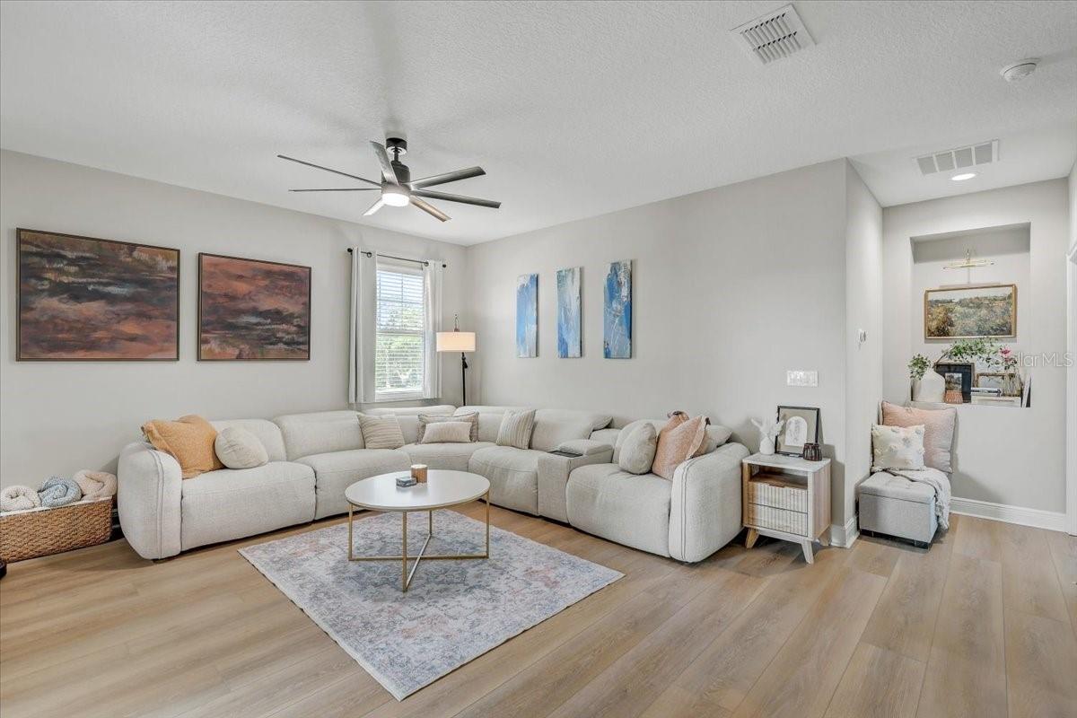 Furnished living room with a large sectional, ceiling fan, and light wood flooring.