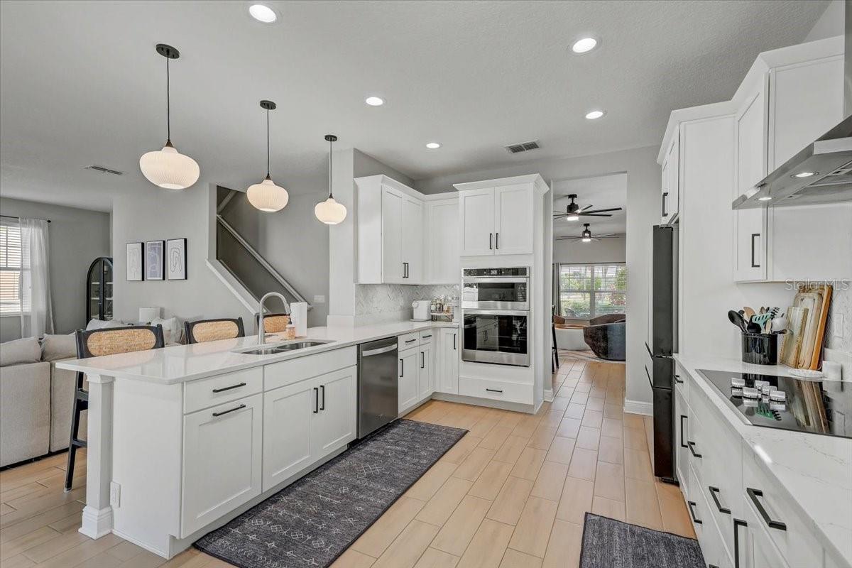 White kitchen with a large island, stainless steel appliances, and pendant lights beside a dining nook.