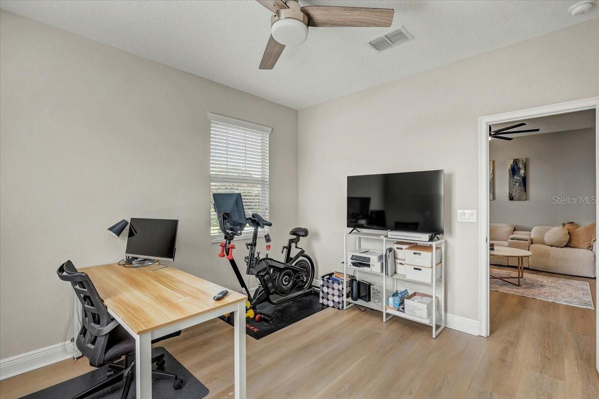 Home office with a wood desk, exercise bike, and television beside a doorway to the living room.