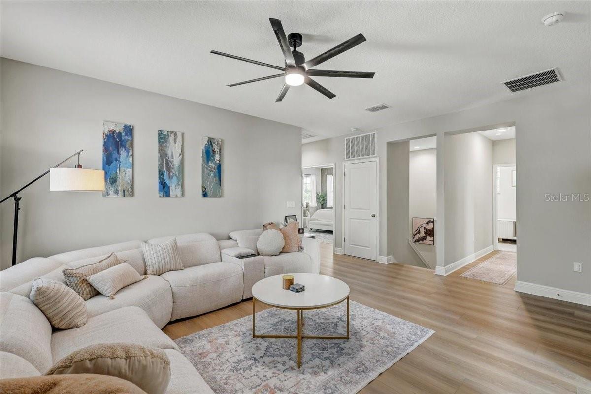 Staged living room with a cream sectional, patterned rug, and modern ceiling fan.