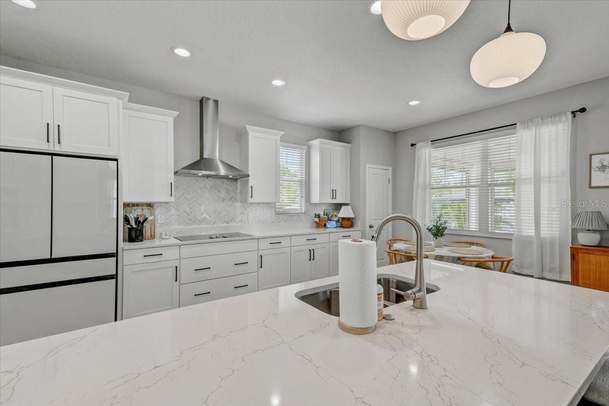 Bright white kitchen with a large veined island, stainless steel appliances, and a window-side dining nook.