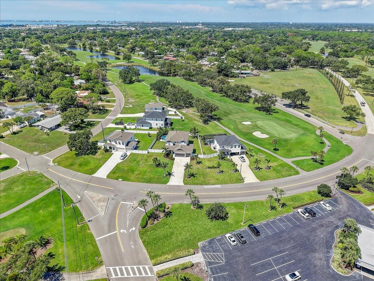 Aerial view of homes beside a golf course with ponds and a distant coastal skyline.