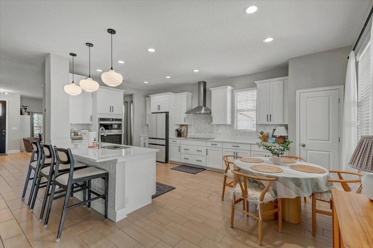 Open-plan kitchen with white cabinetry, stainless steel appliances, and a large island beside a round dining table.