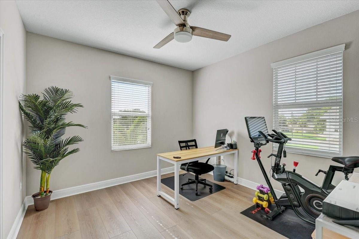 Home office and workout room with a desk, exercise bike, treadmill, and two windows.