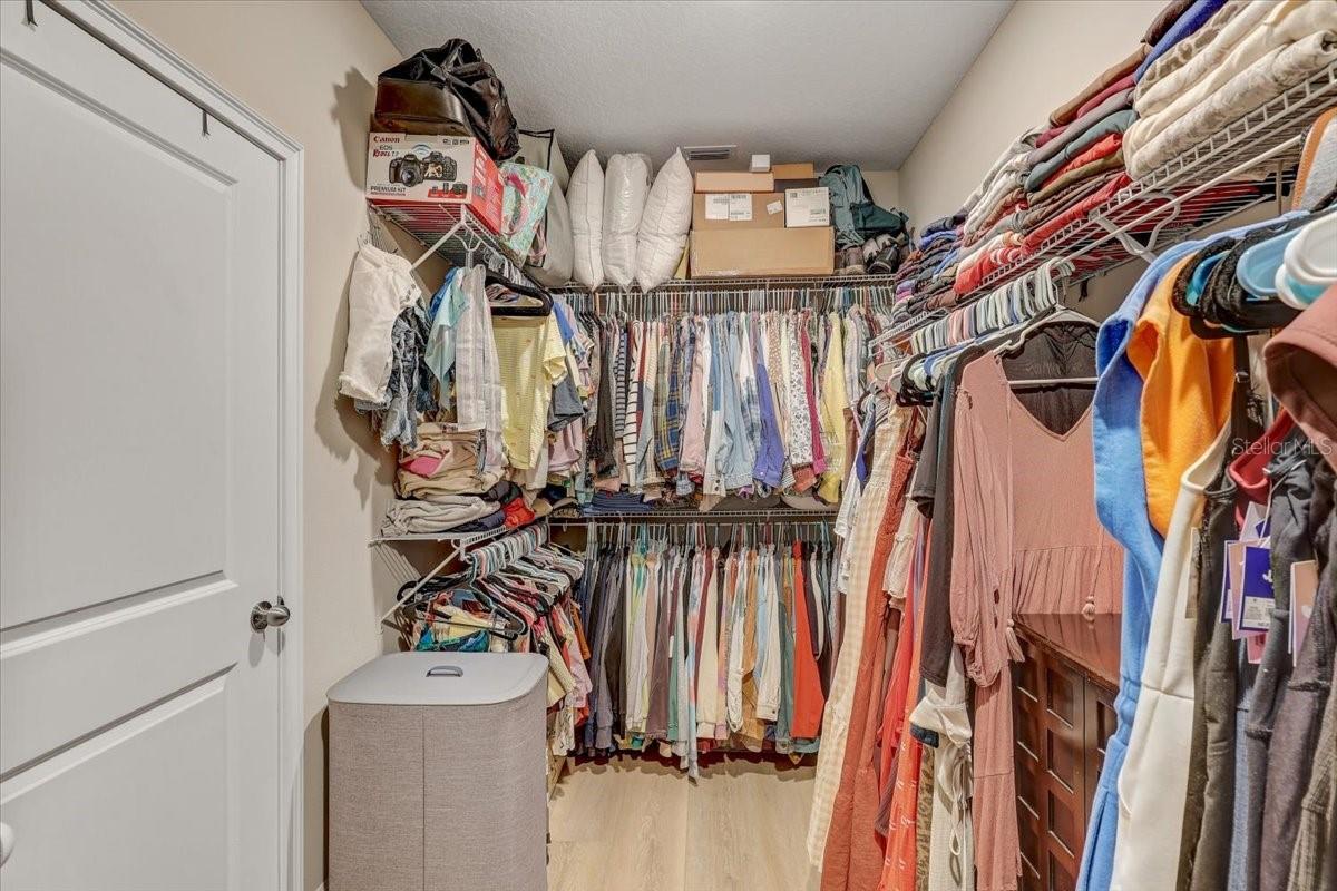 Walk-in closet with clothes on three walls, storage boxes overhead, and a laundry hamper.