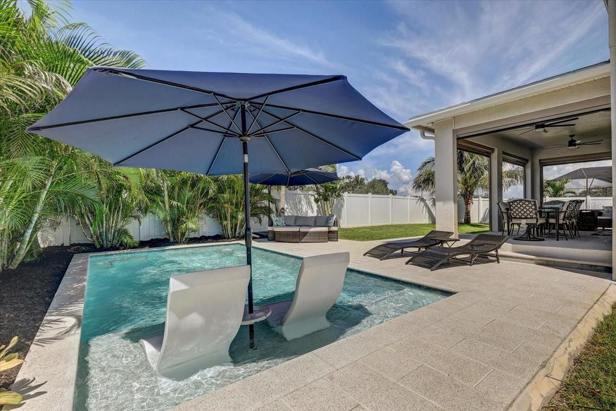 Backyard pool with in-water loungers, navy umbrella, and covered outdoor dining patio.
