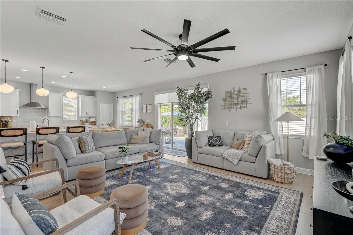 Furnished living room with gray sofas, patterned rug, and open white kitchen.