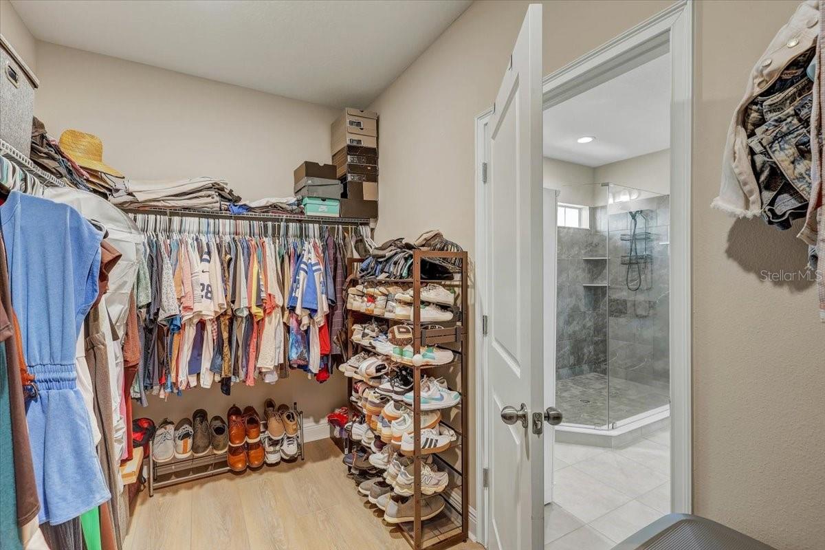 Walk-in closet packed with clothes and shoes, opening onto a tiled bathroom with a glass shower.