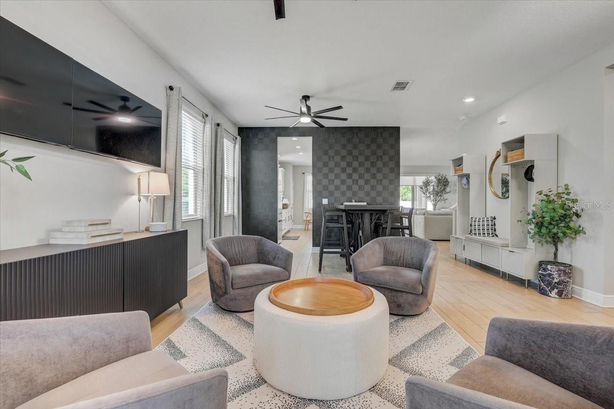 Open-plan living room with gray accent chairs, a round coffee table, and a dark patterned dining-area wall.