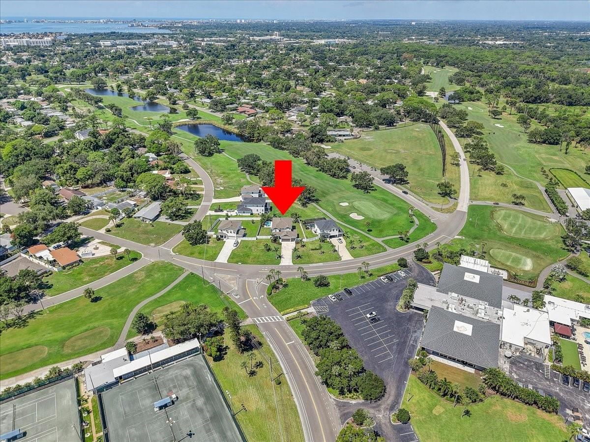 Aerial view of the home marked by a red arrow beside golf course fairways and ponds.