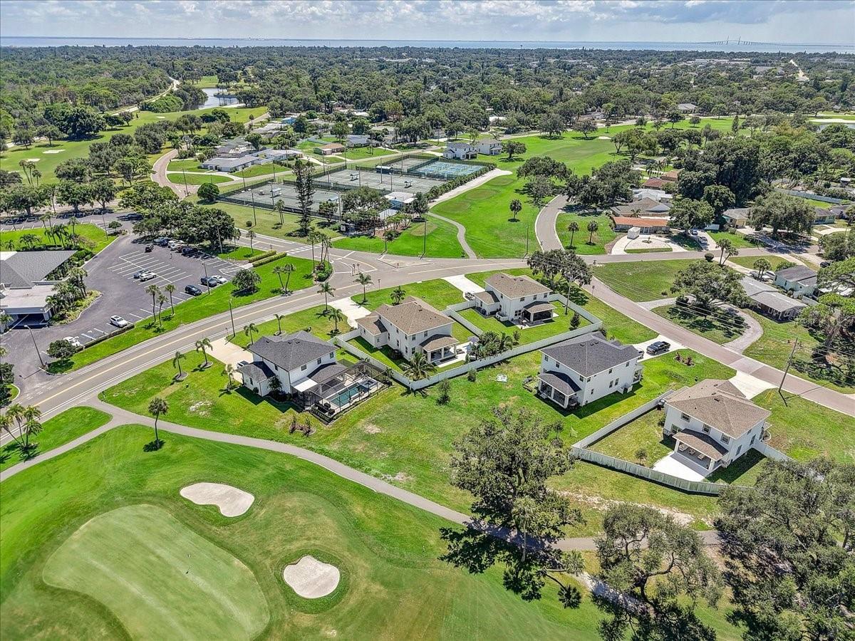 Aerial view of homes beside a golf course, with tennis courts and neighborhood streets.