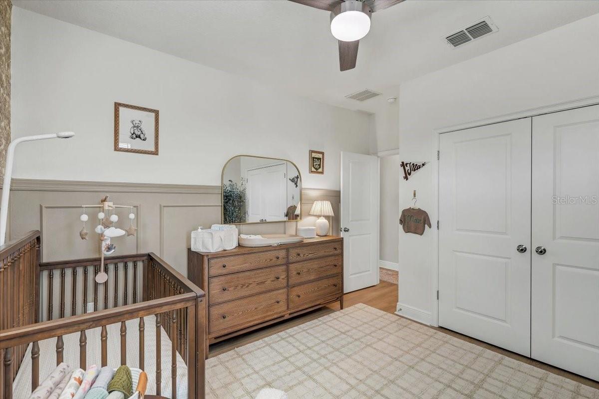 Nursery with a wooden crib beside a changing dresser and white double closet doors.