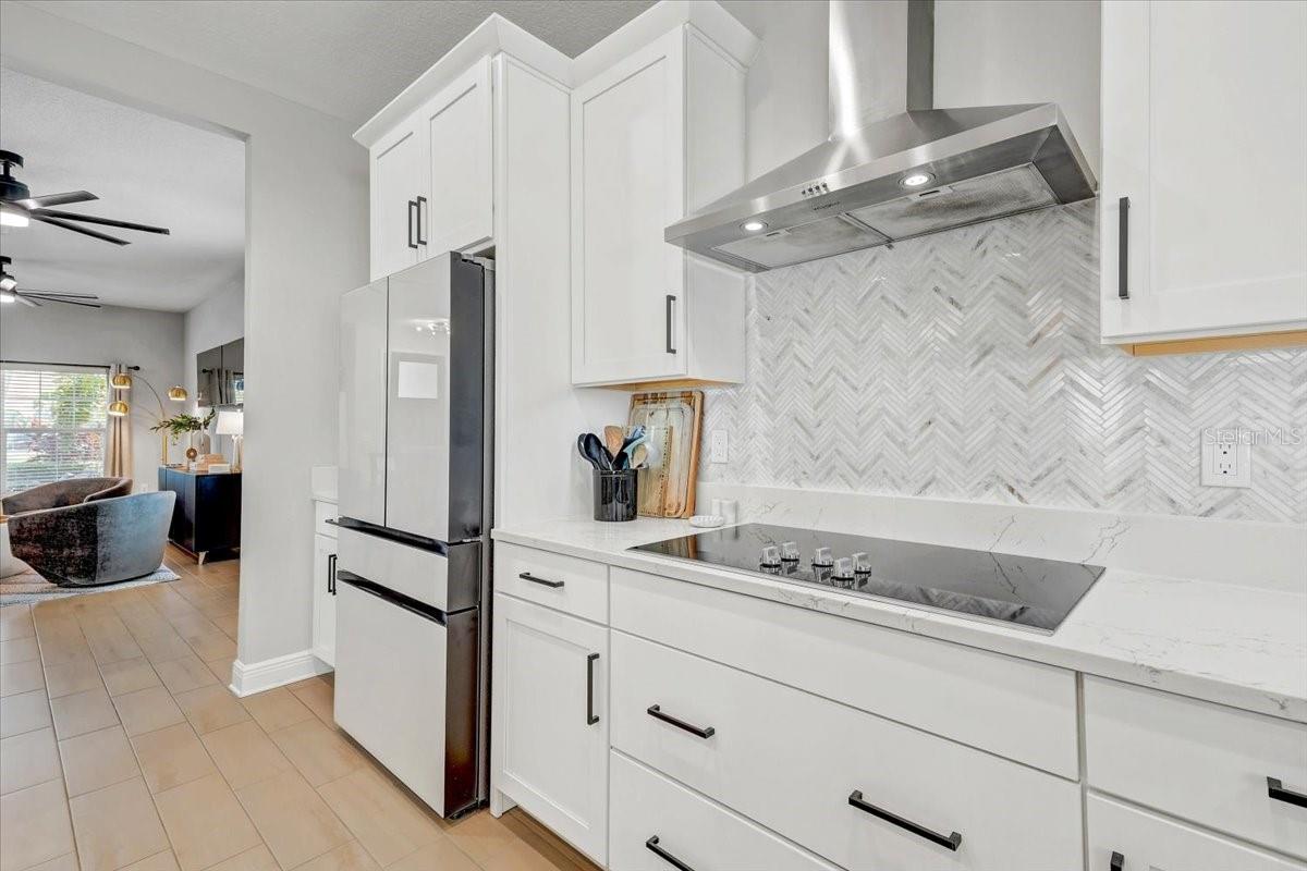 Kitchen with white cabinets, stainless steel appliances, and a gray herringbone backsplash opening to the living area.