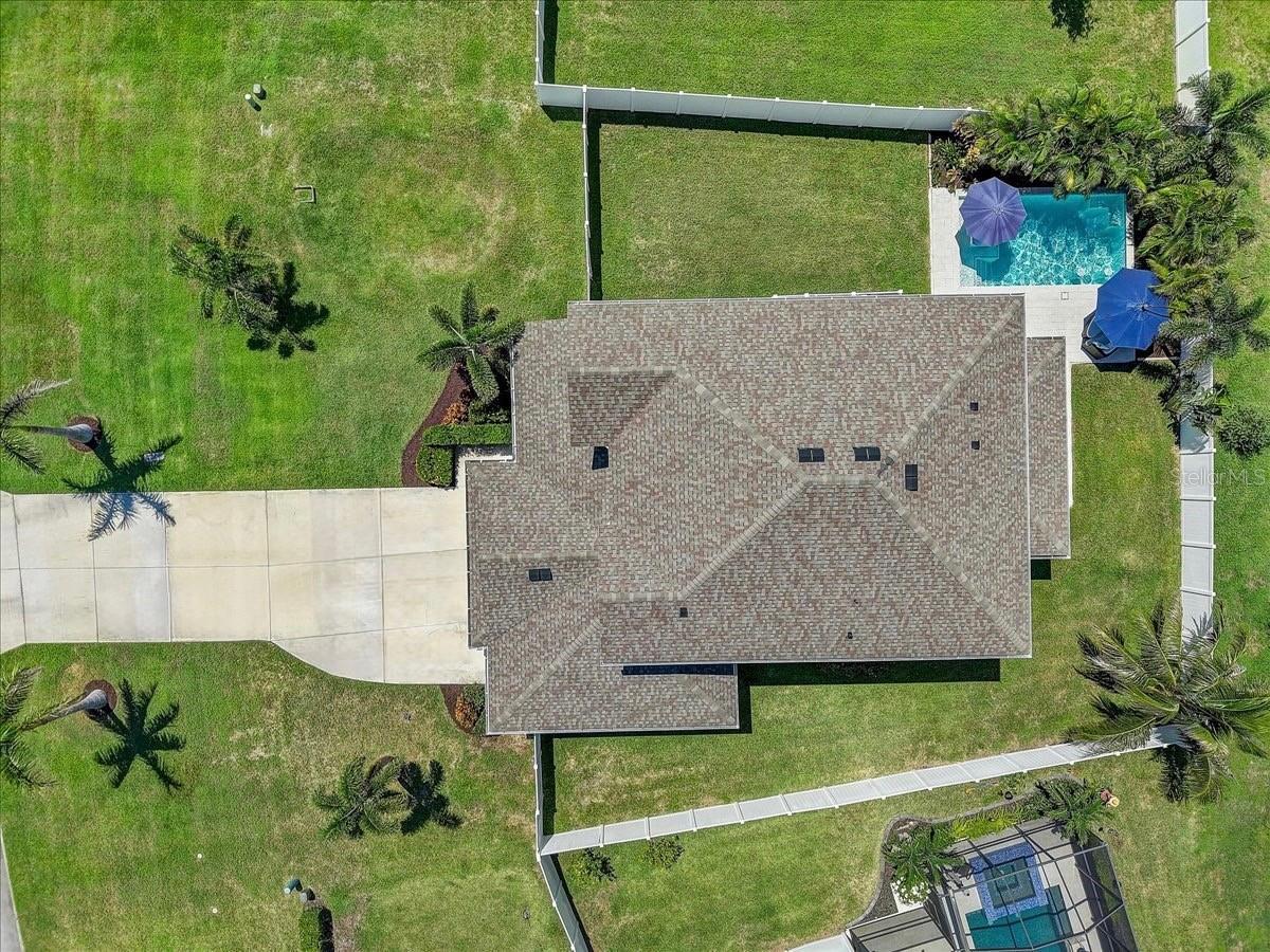 Aerial view of a house with a fenced lawn, driveway, and backyard swimming pool.