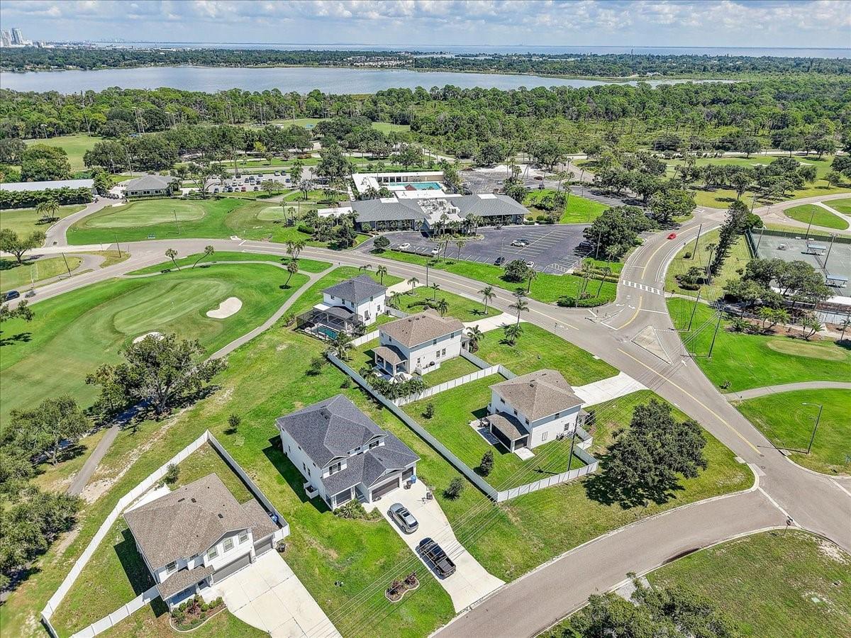 Aerial view of homes beside a golf course, clubhouse, pool, and broad bay.