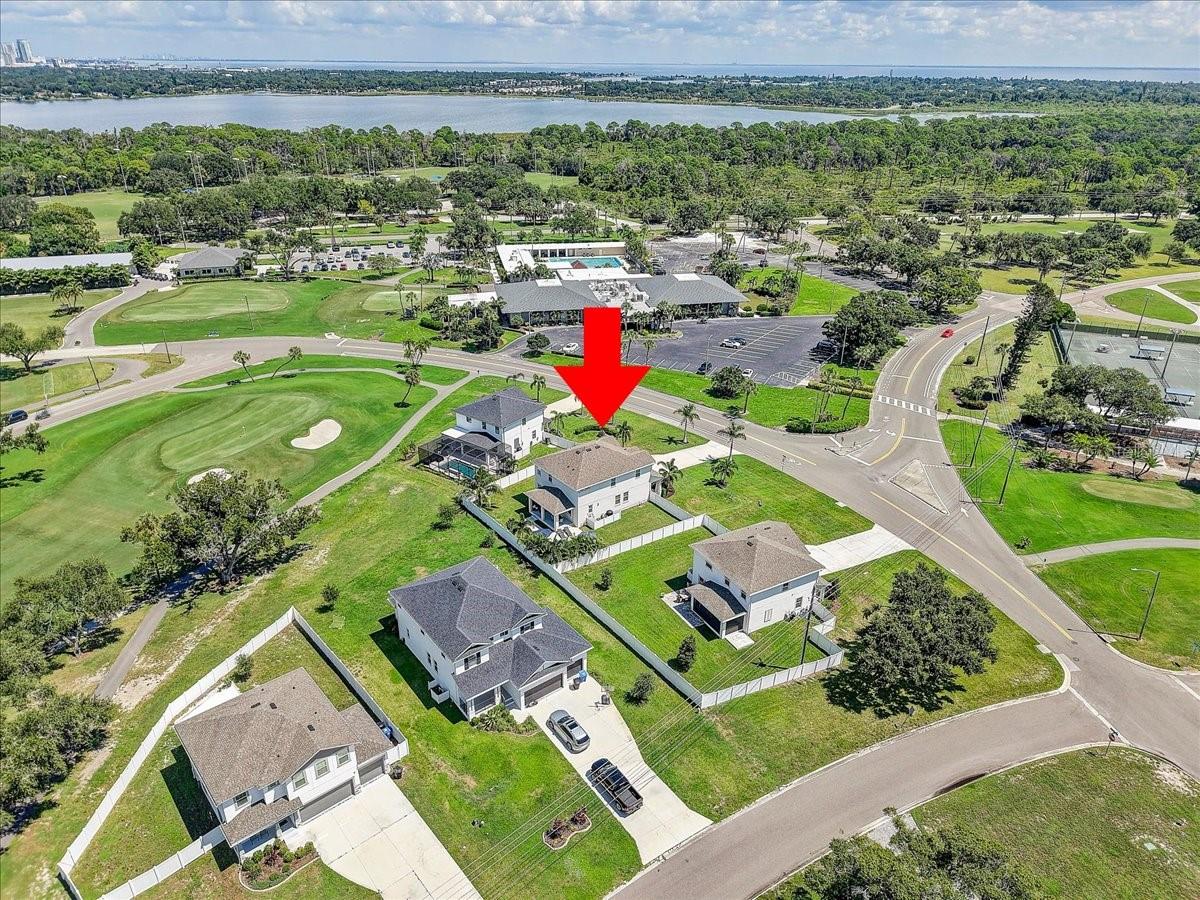 Aerial view of a home beside a golf course, with water visible in the distance.
