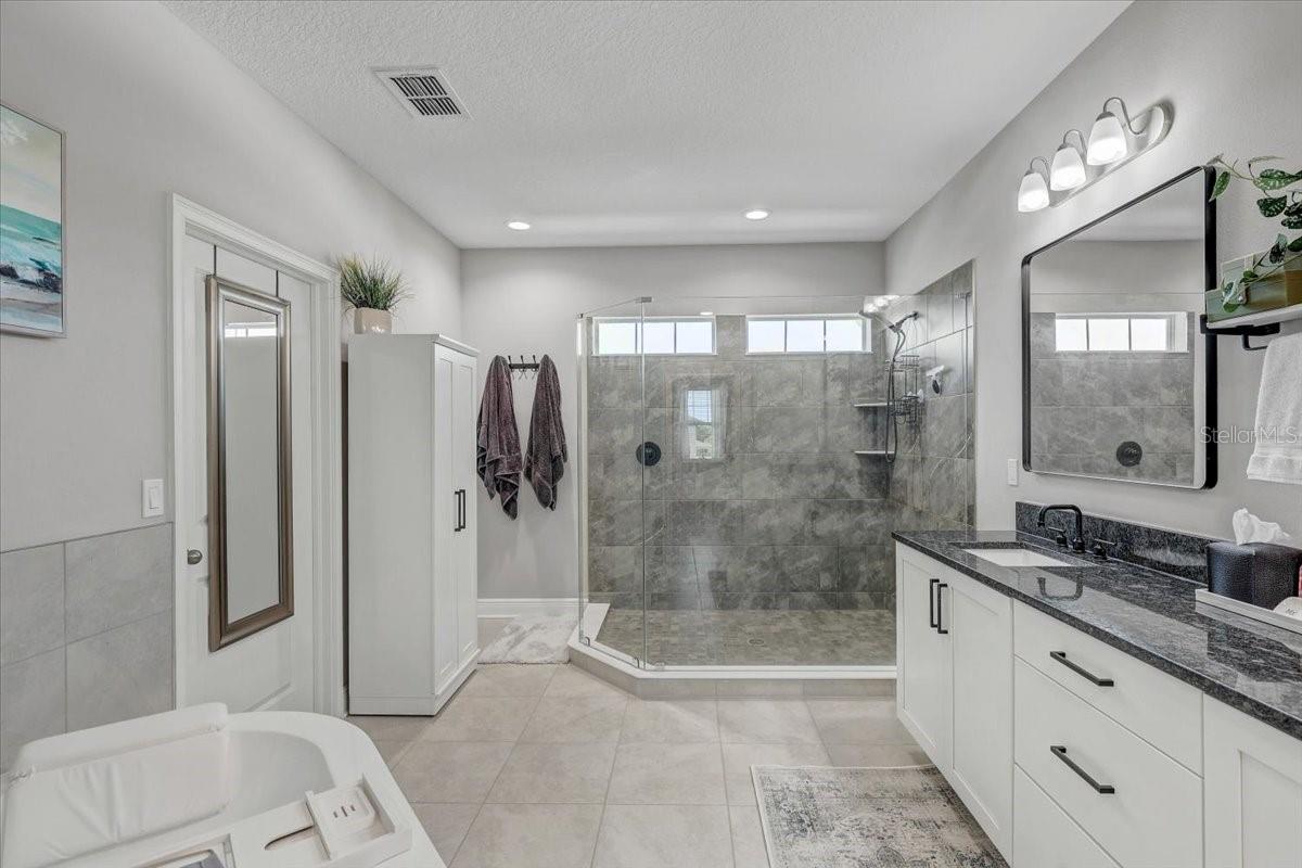 Bathroom with a glass-enclosed gray-tile shower, long white vanity, and soaking tub.