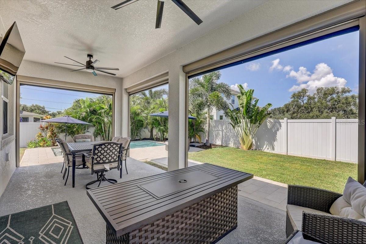 Covered patio with outdoor dining furniture overlooking a fenced lawn and swimming pool.