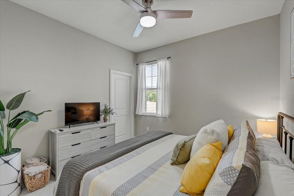 Bedroom with gray and yellow bedding, a television on a light dresser, and a ceiling fan.