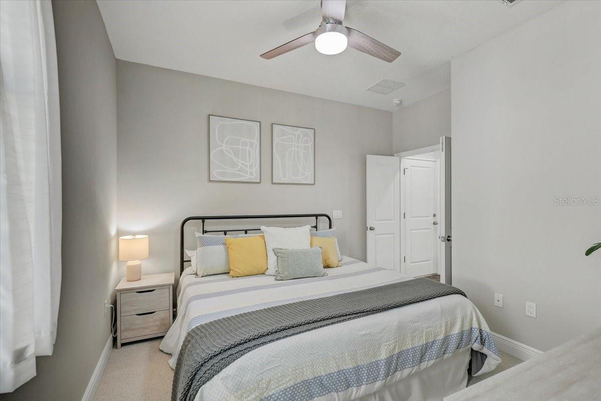 Bedroom with a black metal bed, yellow accent pillows, framed abstract art, and a ceiling fan.
