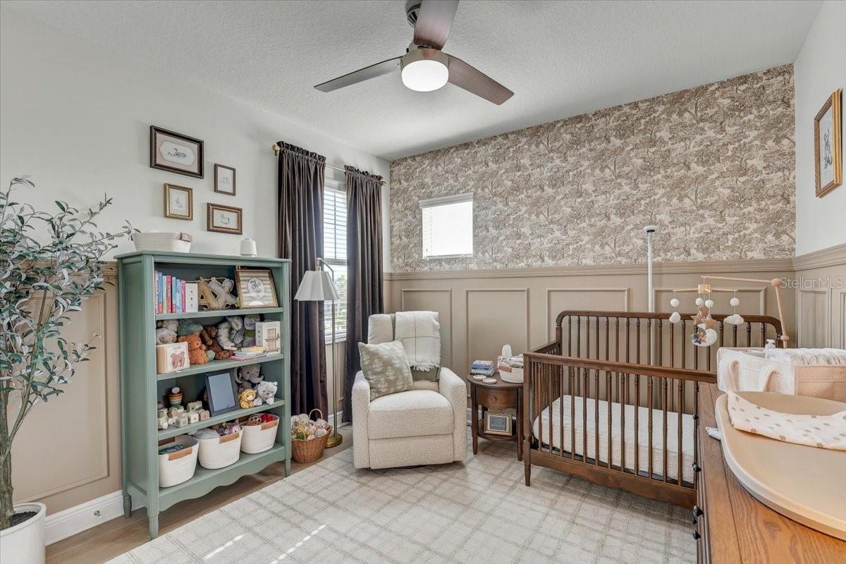 Nursery with a wooden crib, white armchair, and green bookshelf filled with toys.