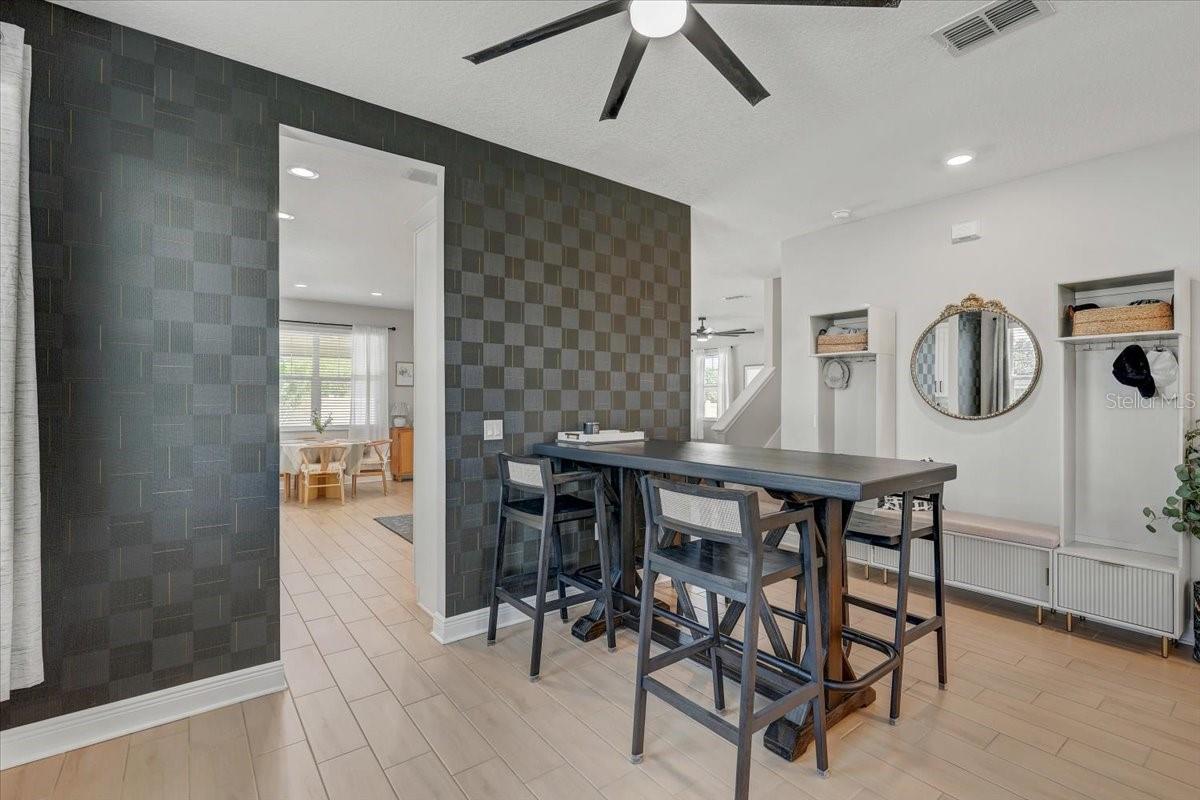 Dining area with a dark tile accent wall, long table, tall chairs, and built-in shelves.