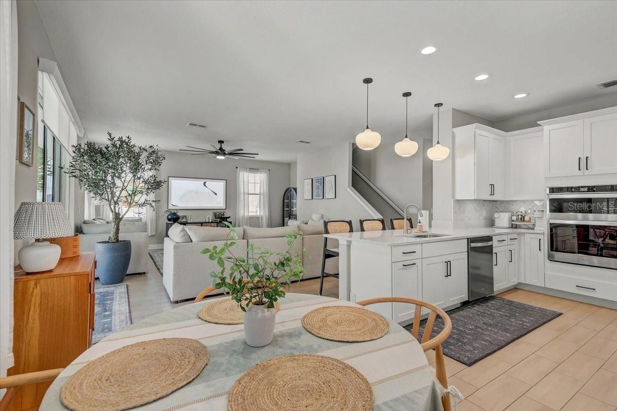 Open-plan kitchen, dining, and living room with a white island, pendant lights, and large windows.