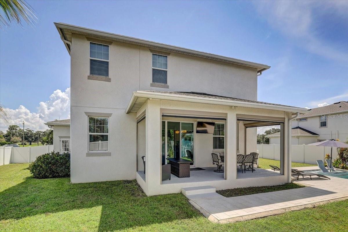 Two-story home with a covered patio, outdoor seating, and a pool beside the fenced lawn.