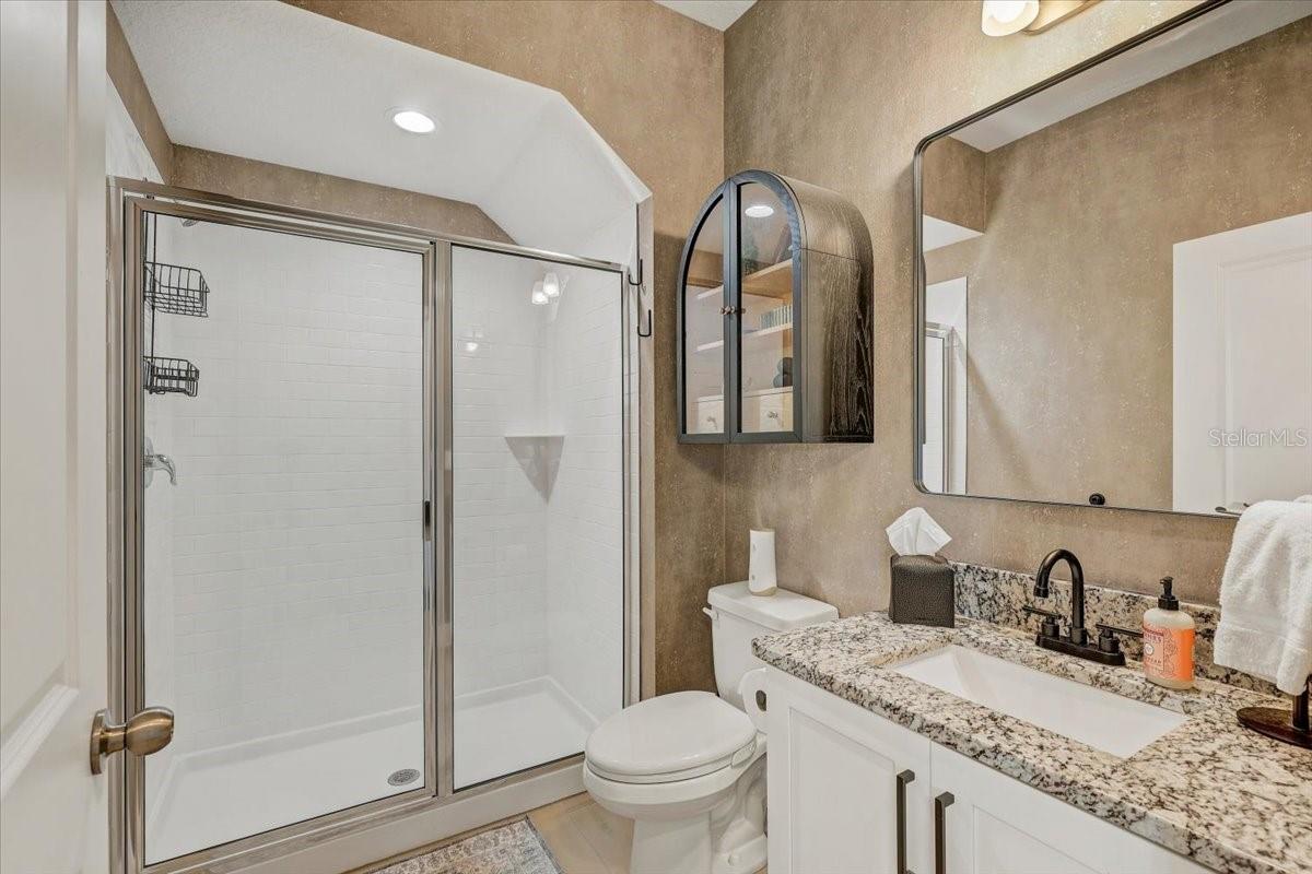 Bathroom with a glass-enclosed tiled shower and granite-topped vanity with black faucet.