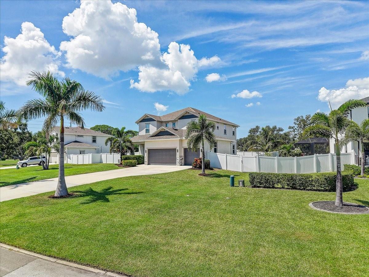 Two-story house with a double garage, white fence, palm trees, and broad green lawn.