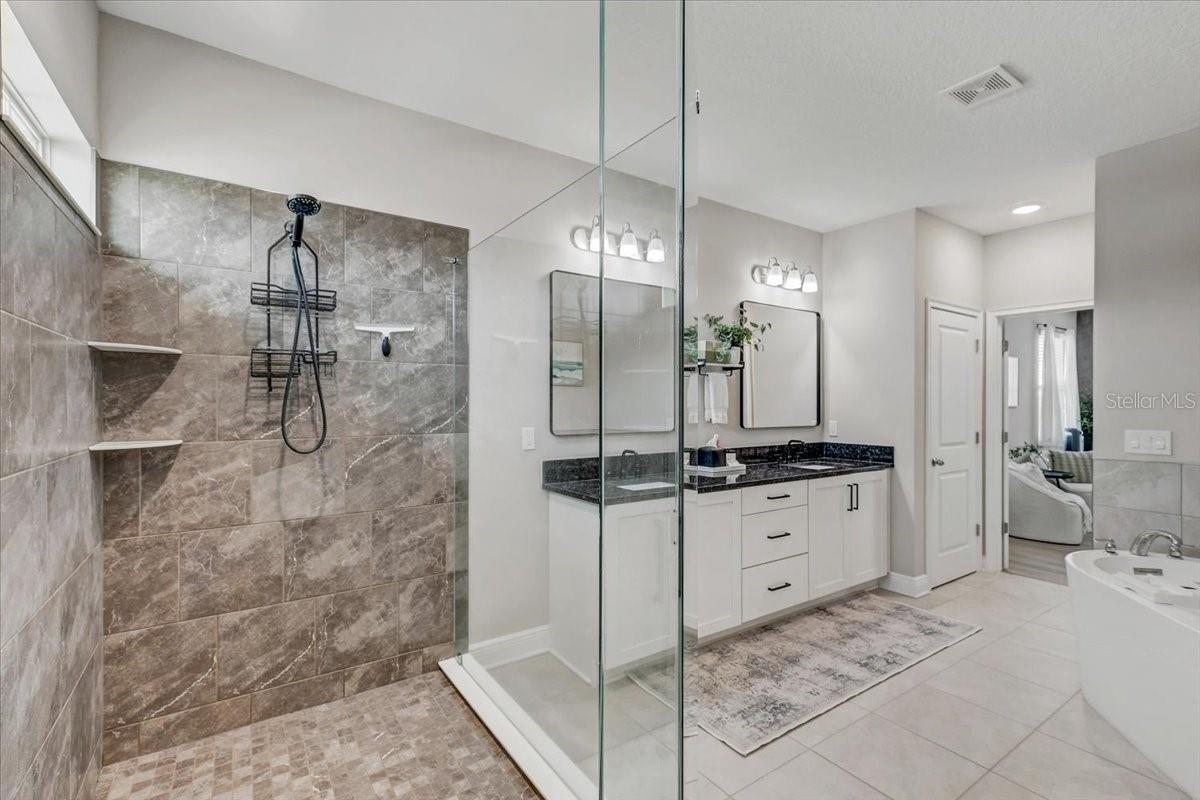 Bathroom with a glass-enclosed tiled shower and white vanity with dark countertop.