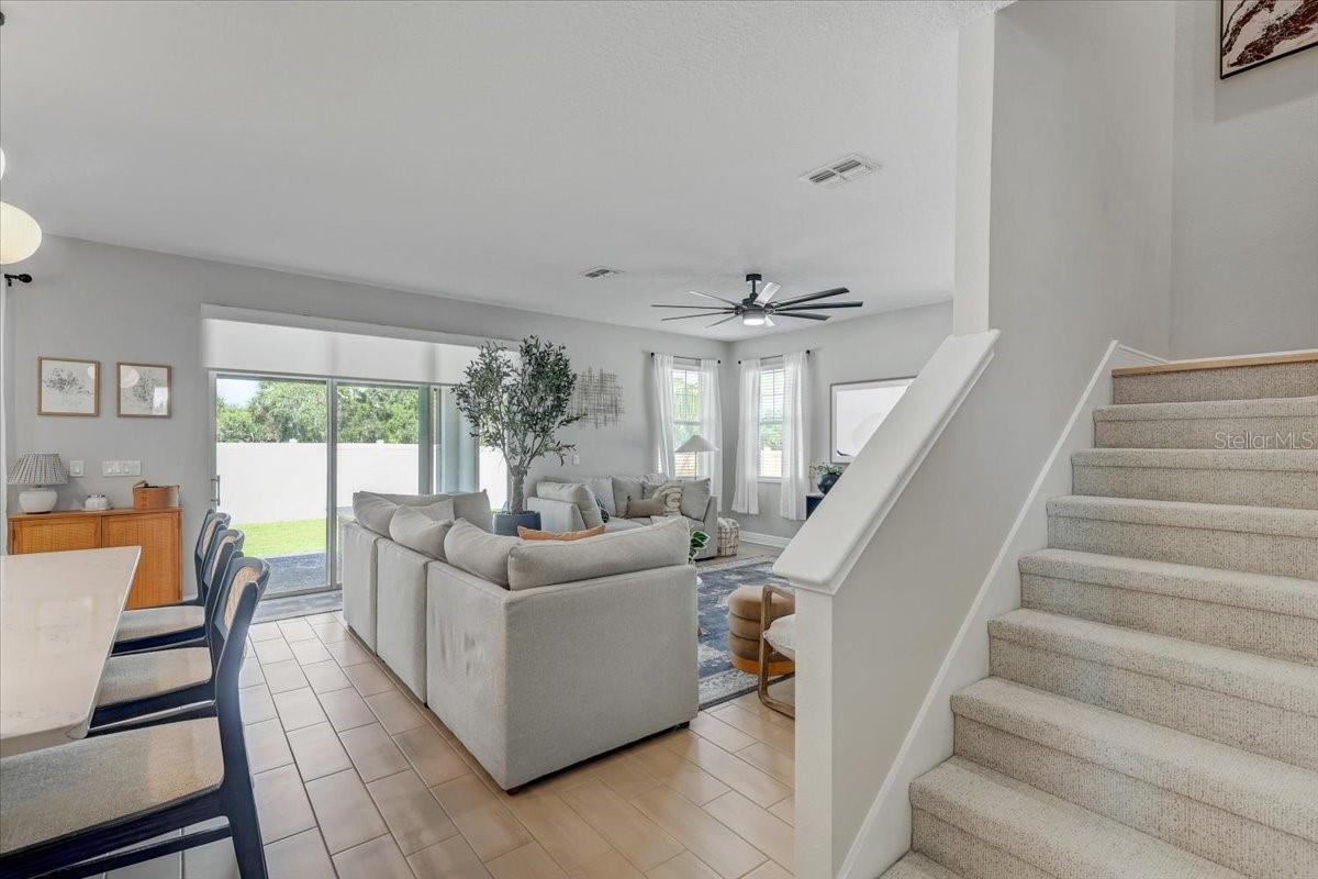 Open-plan living room with pale sofas, a sliding glass door to the lawn, and a carpeted staircase.
