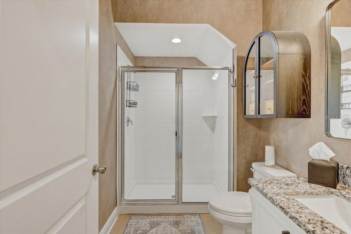 Bathroom with a glass shower, granite vanity, and arched mirrored cabinet.