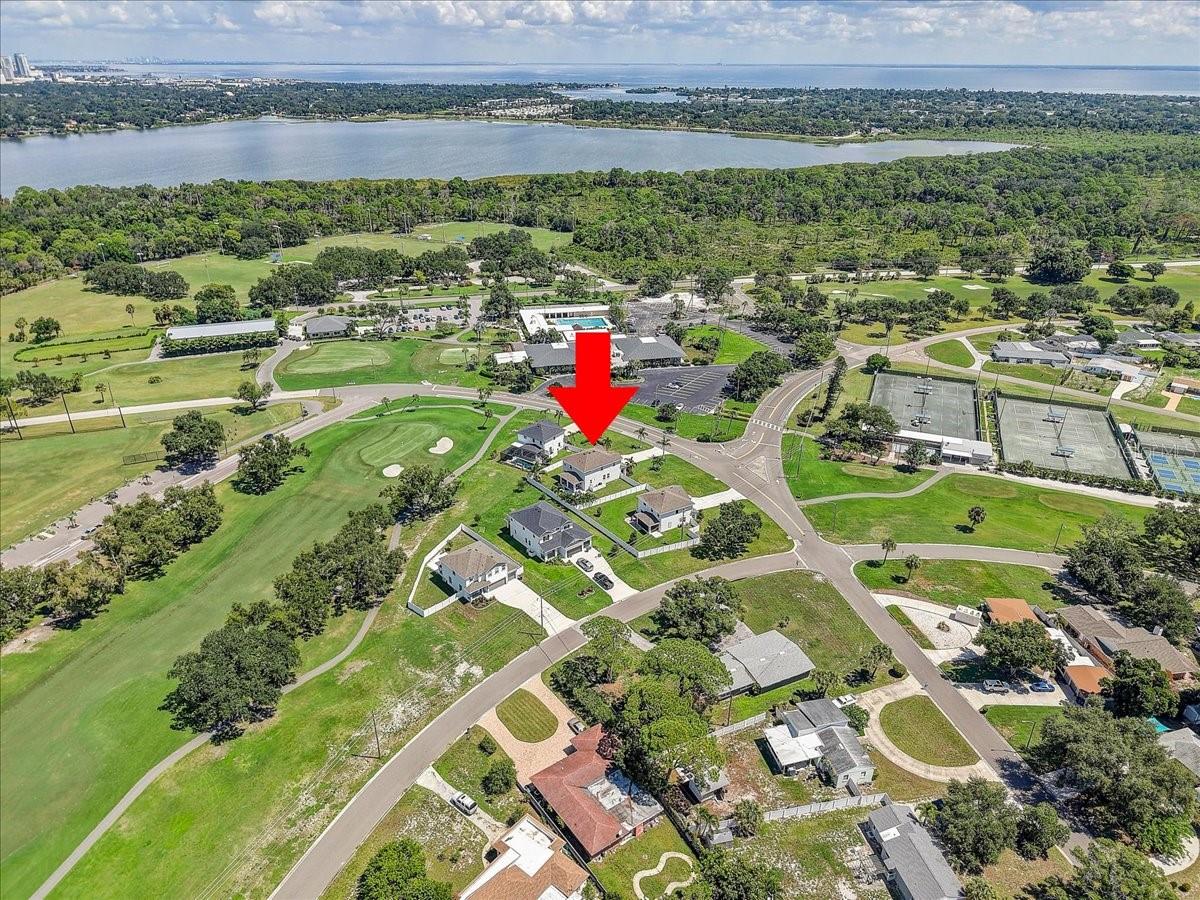 Aerial view of a home marked by a red arrow beside a golf course and bay.