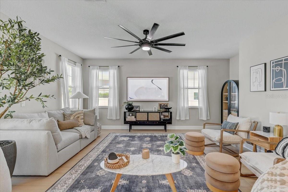 Living room with a white sofa, large curtained windows, patterned rug, and modern ceiling fan.